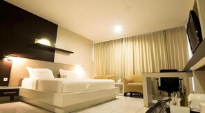 A modern hotel room with a bed, a sofa, a TV, and a desk.