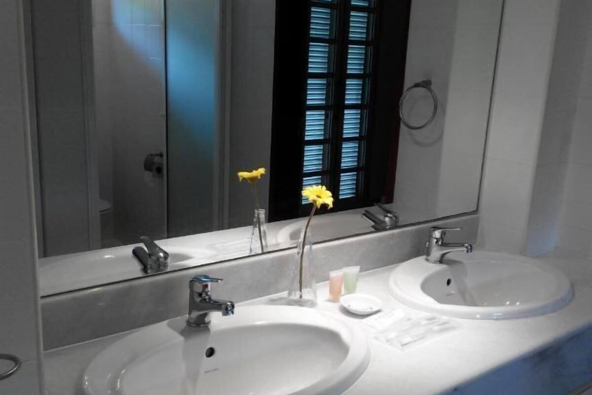 Un baño con dos lavamanos, un espejo grande y una ventana con persianas.
