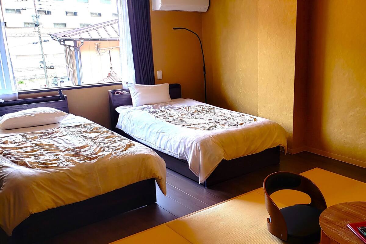 A hotel room with two beds, a desk, a chair, a lamp, and a TV.
