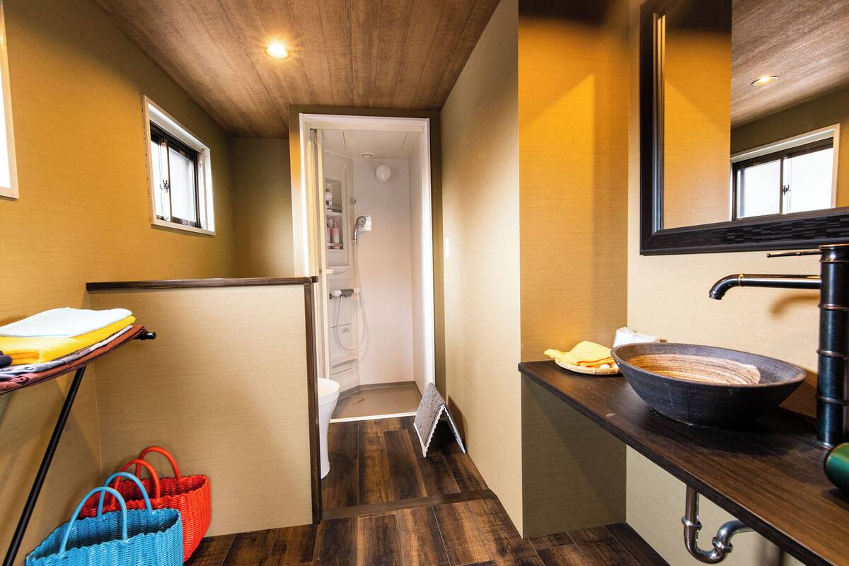 A bathroom with a wooden floor, a sink with a large bowl, a mirror, and a shower area.