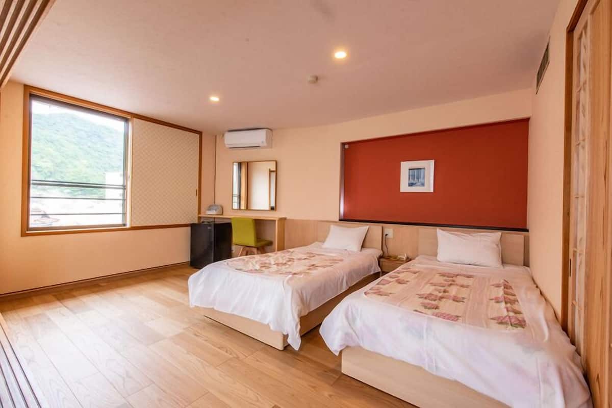 A hotel room with two beds, a desk, a chair, a window with a view, and a red accent wall.