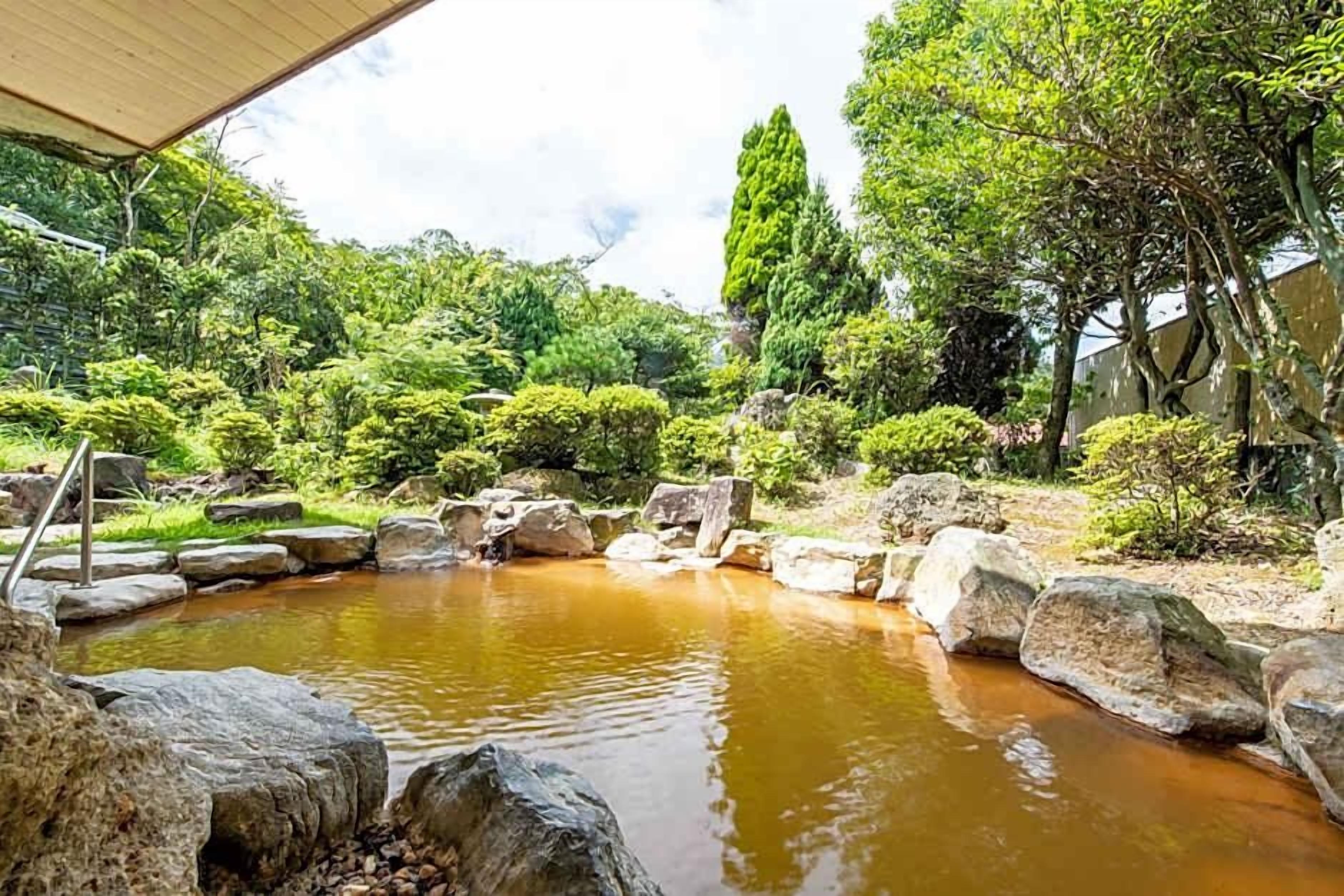 A tranquil garden with a pond, surrounded by rocks and lush greenery.