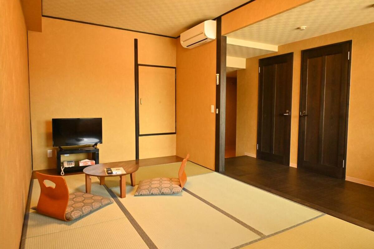 A traditional Japanese room with tatami flooring, a television, a small table, and a sofa.