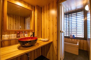 A wooden interior with a large mirror, a wooden countertop, and a window with blinds. - Unzen Sky (UNZEN)