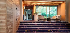 A staircase with floral carpet leading to a seating area with two chairs and a table, surrounded by wooden paneling and large windows. - Unzen Sky (UNZEN)