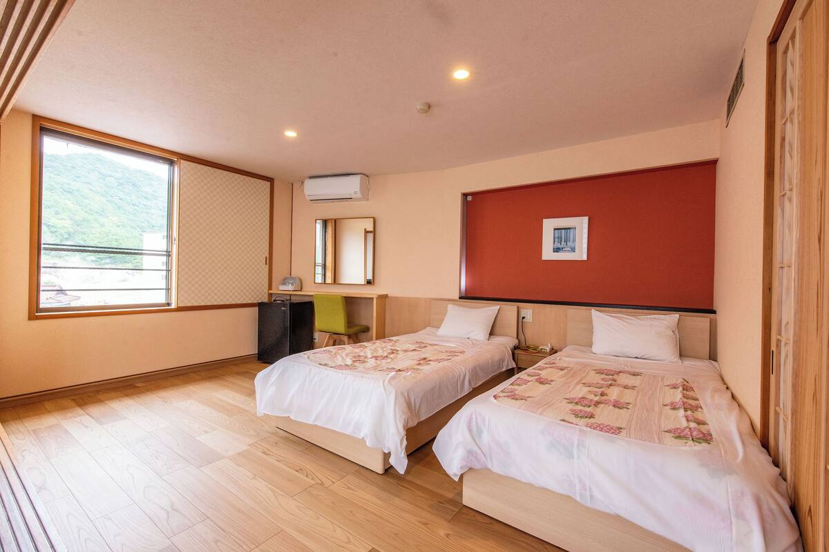 A room with two beds, a desk, a chair, and a window with a view.