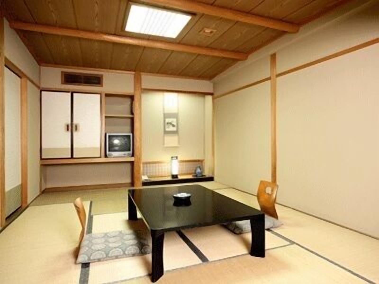 Une pièce de style japonais traditionnel, avec un sol recouvert de tatamis, une table basse, une chaise, un meuble et un téléviseur.