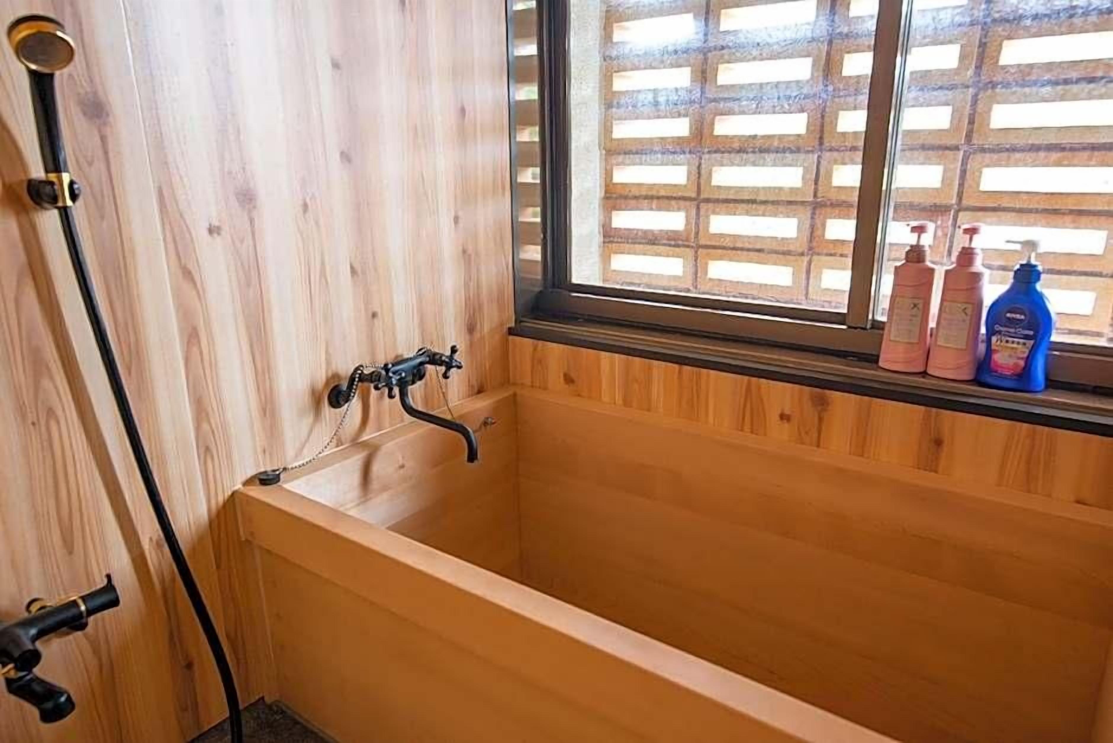 Puinen kylpyamme, jonka yläpuolella on ikkuna, suihkupää ja kaksi shampoopulloa ikkunalaudalla.