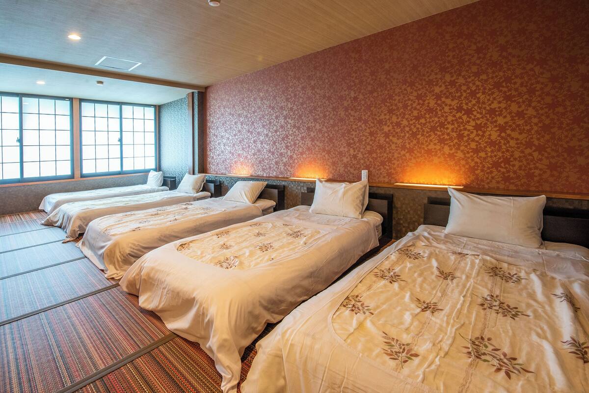 A hotel room with three beds, large windows, and a patterned wall.