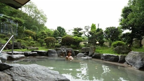 A person in a natural pool surrounded by rocks and greenery. - Unzen Sky (UNZEN)