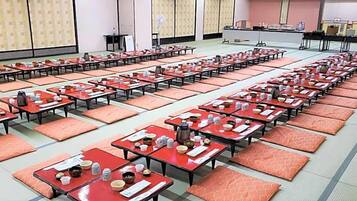 Un salón amplio con filas de mesas y sillas, algunas con objetos encima, y un escenario al fondo.