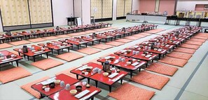 A large room with rows of tables and chairs, some with items on them, and a stage area in the background. - Unzen Sky (UNZEN)