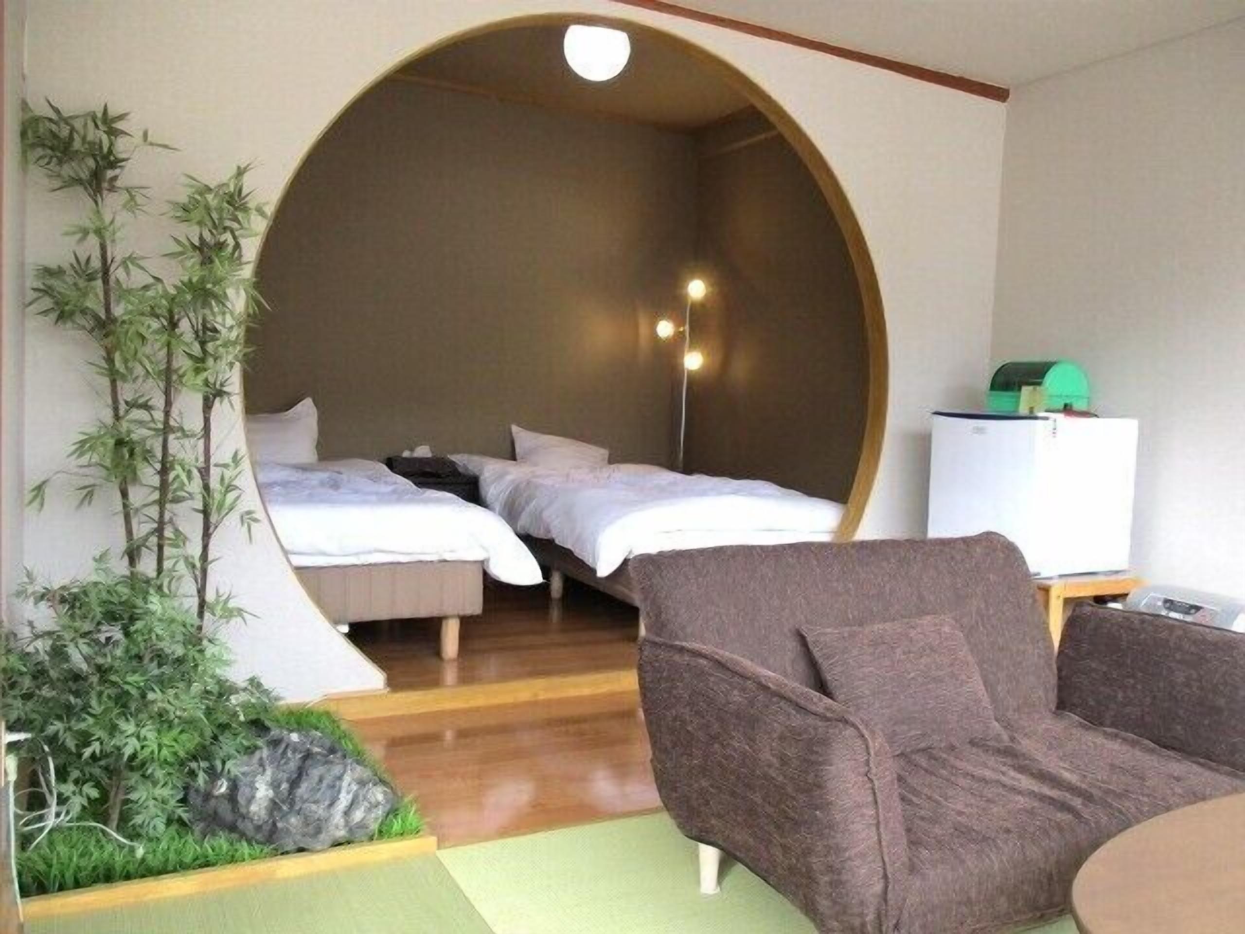 A room with two beds, a sofa, a small table, a refrigerator, and a wall-mounted light fixture.