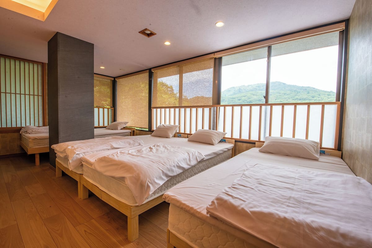 A hotel room with two beds, a large window with a view of hills, and a traditional sliding door.