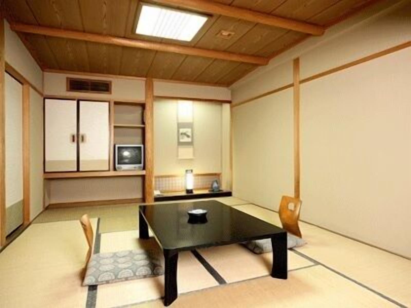 A traditional Japanese-style room with tatami flooring, a low table, a chair, a cabinet, and a television.