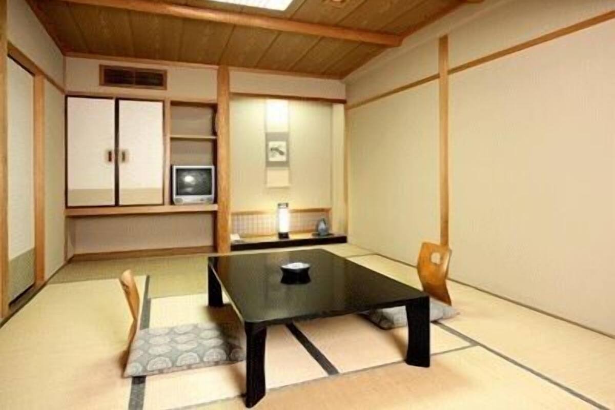 A traditional Japanese-style room with tatami flooring, a low table, a chair, a cabinet, and a television.