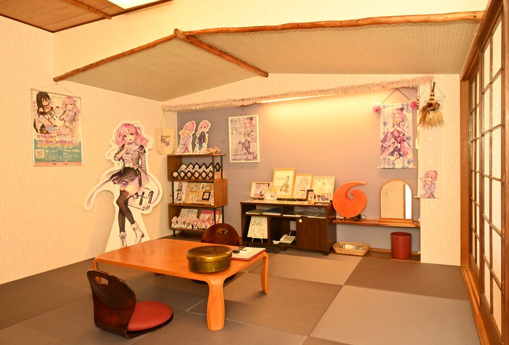 A room with tatami flooring, a wooden table, a chair, and various posters and decorations on the walls.