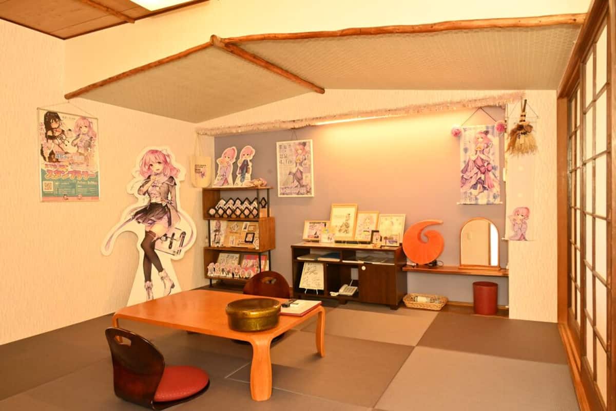 A room with tatami flooring, a wooden table, a chair, and various posters and decorations on the walls.