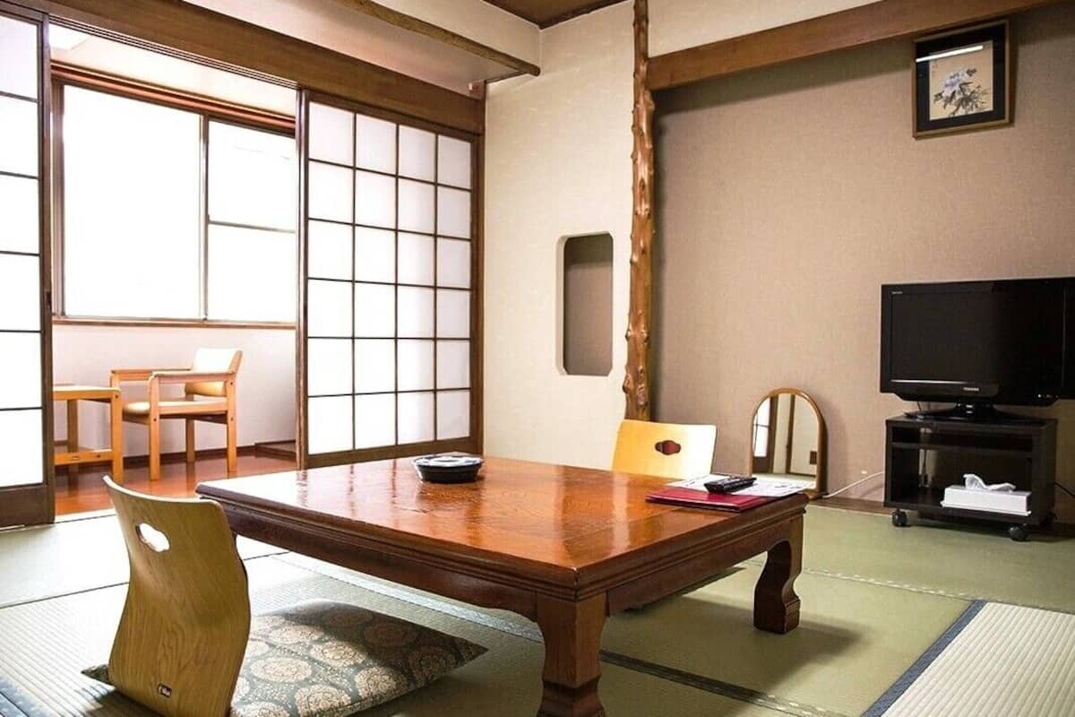 A traditional Japanese room with tatami flooring, a wooden dining table, a television, and a sliding door.