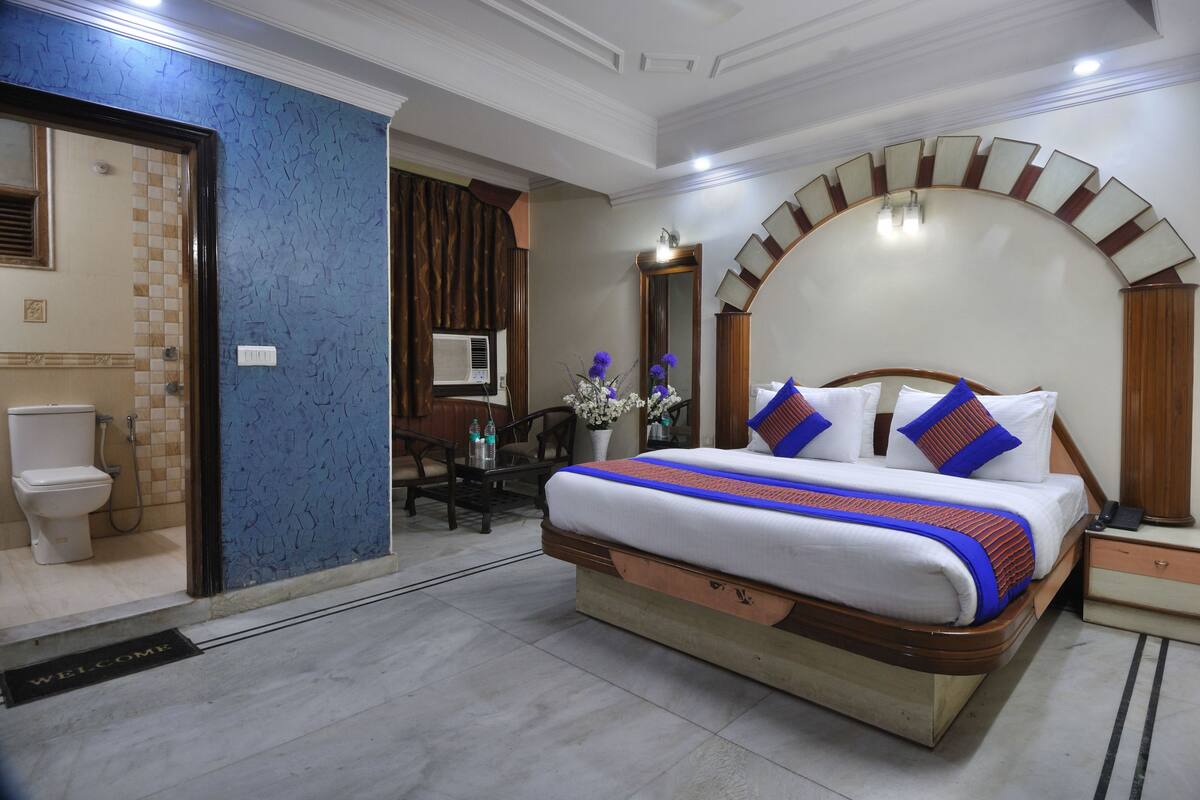 Ein Hotelzimmer mit einem großen Bett, einem Badezimmer mit Toilette und Dusche sowie einem Essbereich mit Tisch und Stühlen.