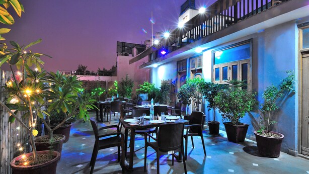 An outdoor dining area with tables and chairs, surrounded by potted plants, under a night sky. - Hotel De Holiday International (New Delhi)