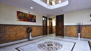 A lobby with a marble floor, a large painting, and a staircase. - Hotel De Holiday International (New Delhi)