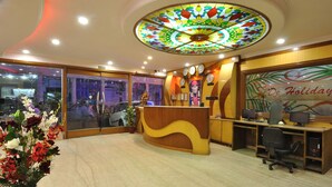 A hotel reception area with a wooden reception desk, a clock, and a stained glass ceiling. - Hotel De Holiday International (New Delhi)