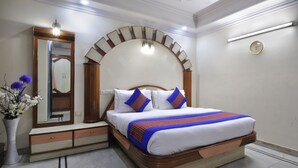 A neatly arranged bedroom with a bed, bedside table, mirror, and a vase of flowers. - Hotel De Holiday International (New Delhi)