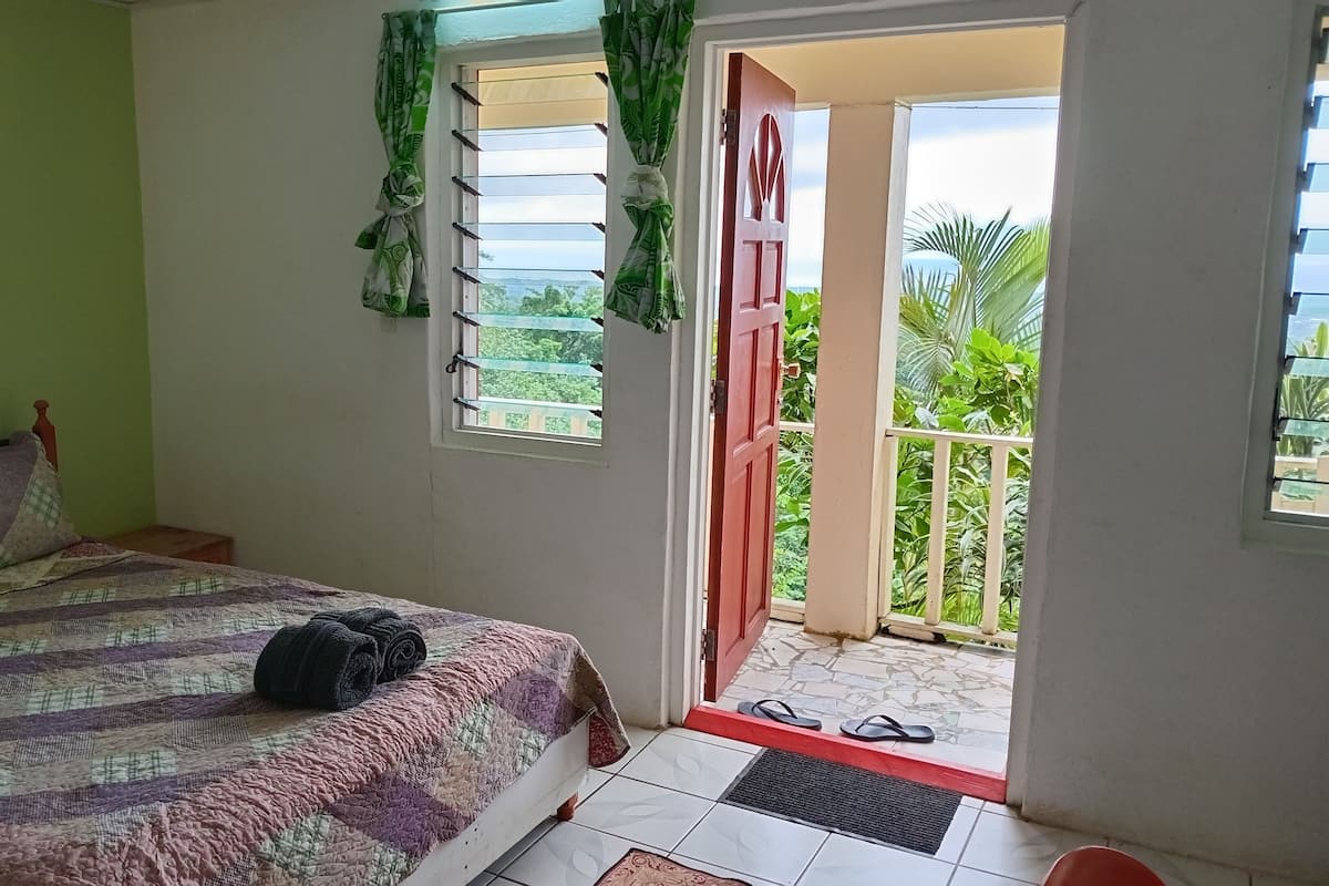 A bedroom with a bed, a window with curtains, and a door leading to an outdoor area.