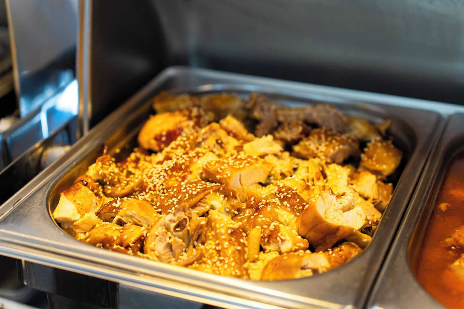 A buffet with various dishes, including chicken and other meats, garnished with sesame seeds.