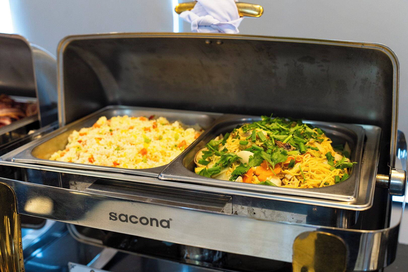 A buffet with two dishes: one appears to be fried rice and the other a noodle dish with vegetables and herbs.