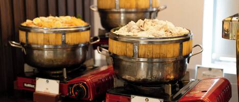 A buffet with various dishes, including Vietnamese steamed rice rolls, served in wooden bowls on electric stoves.