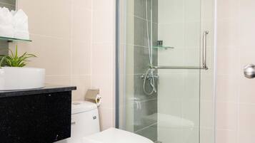 A modern bathroom with a glass-enclosed shower, a white toilet, and a black countertop with a plant.
