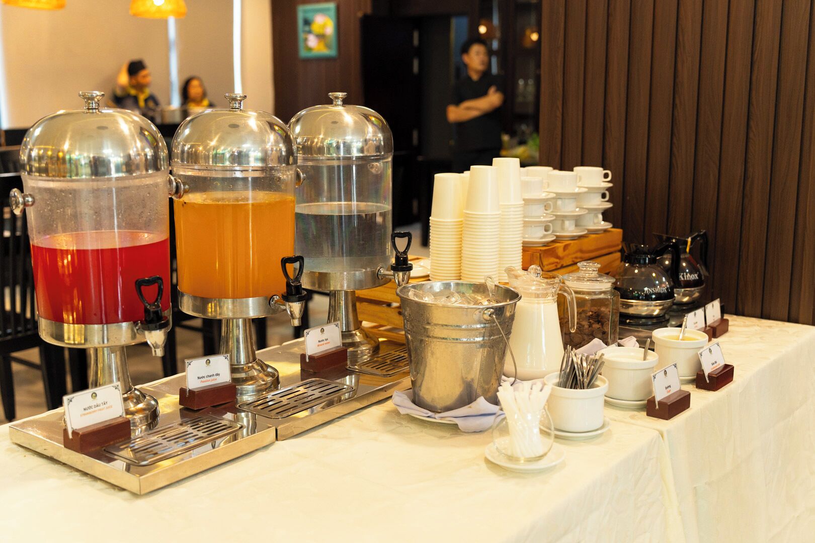 Montaje tipo bufé con dispensadores de bebidas, platos y cubiertos.