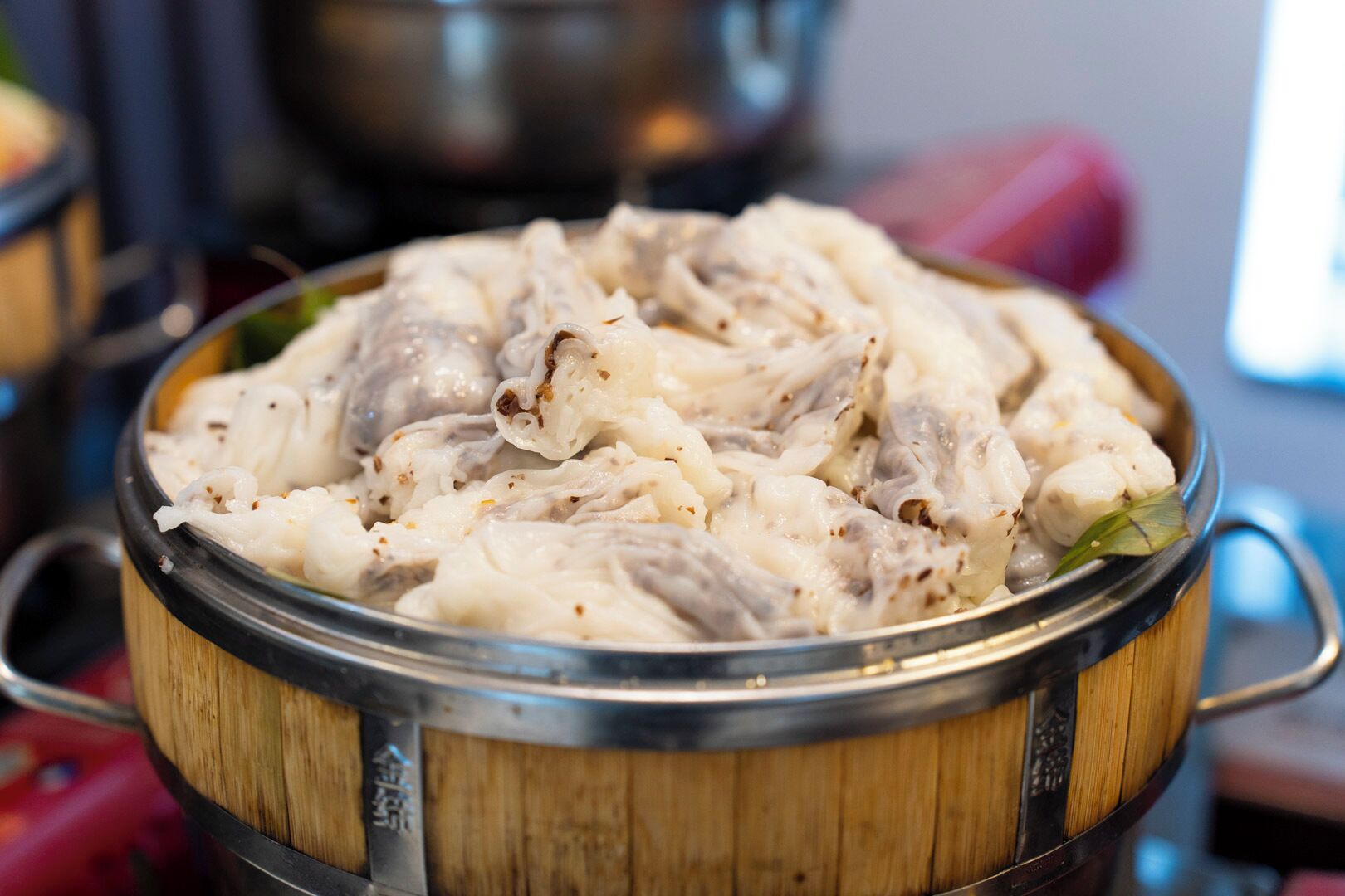 Una vaporera de bambú llena de comida al vapor, probablemente dumplings o bollos, sobre una mesa.