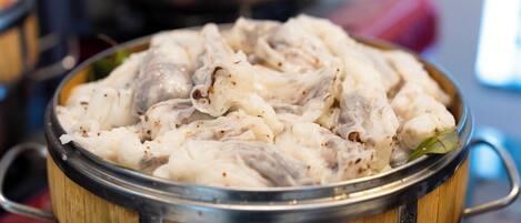 Una vaporera de bambú llena de comida al vapor, probablemente dumplings o bollos, sobre una mesa.