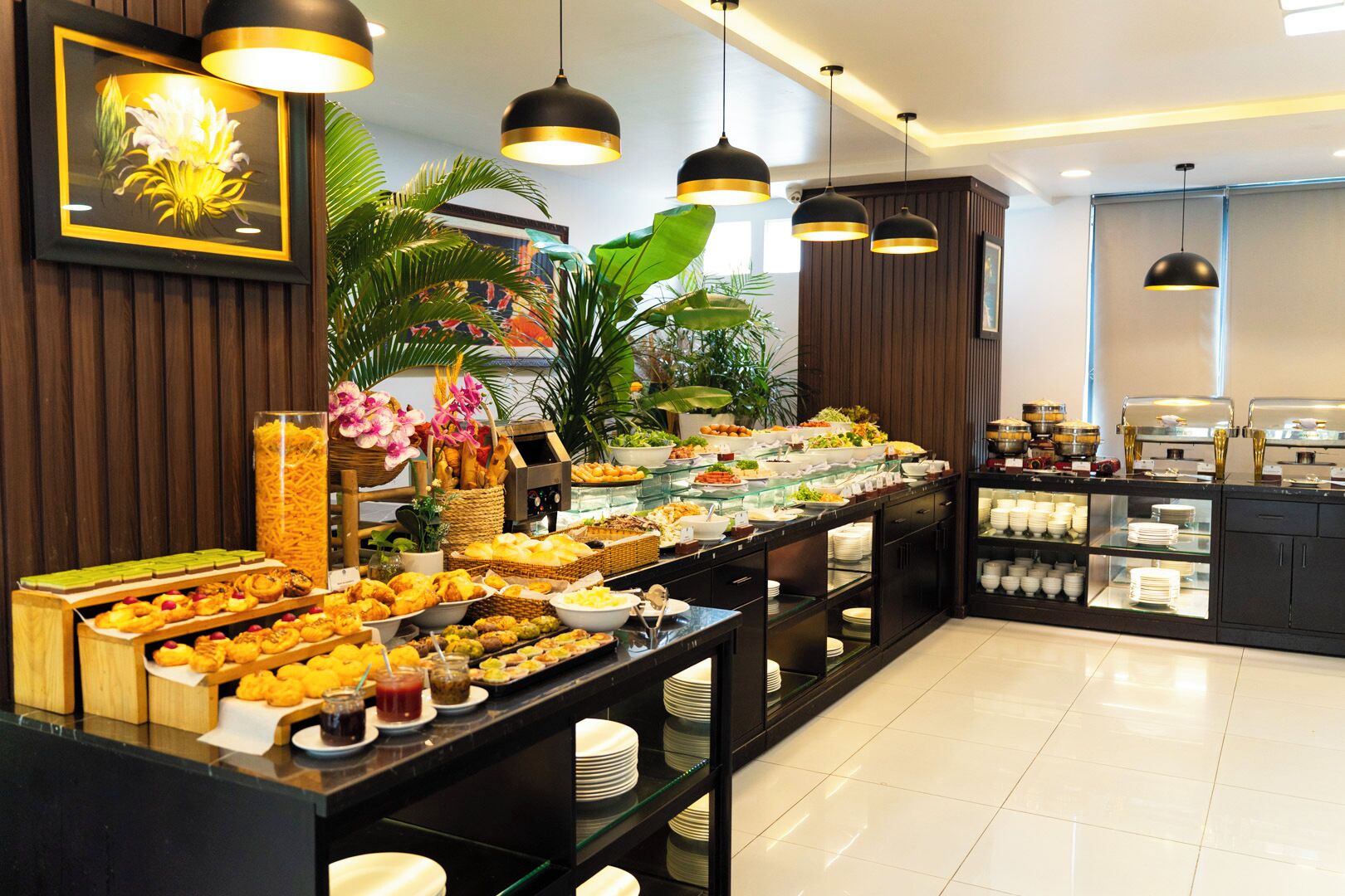 A buffet with various food items, including pastries and salads, in a modern setting with wooden paneling and pendant lighting.