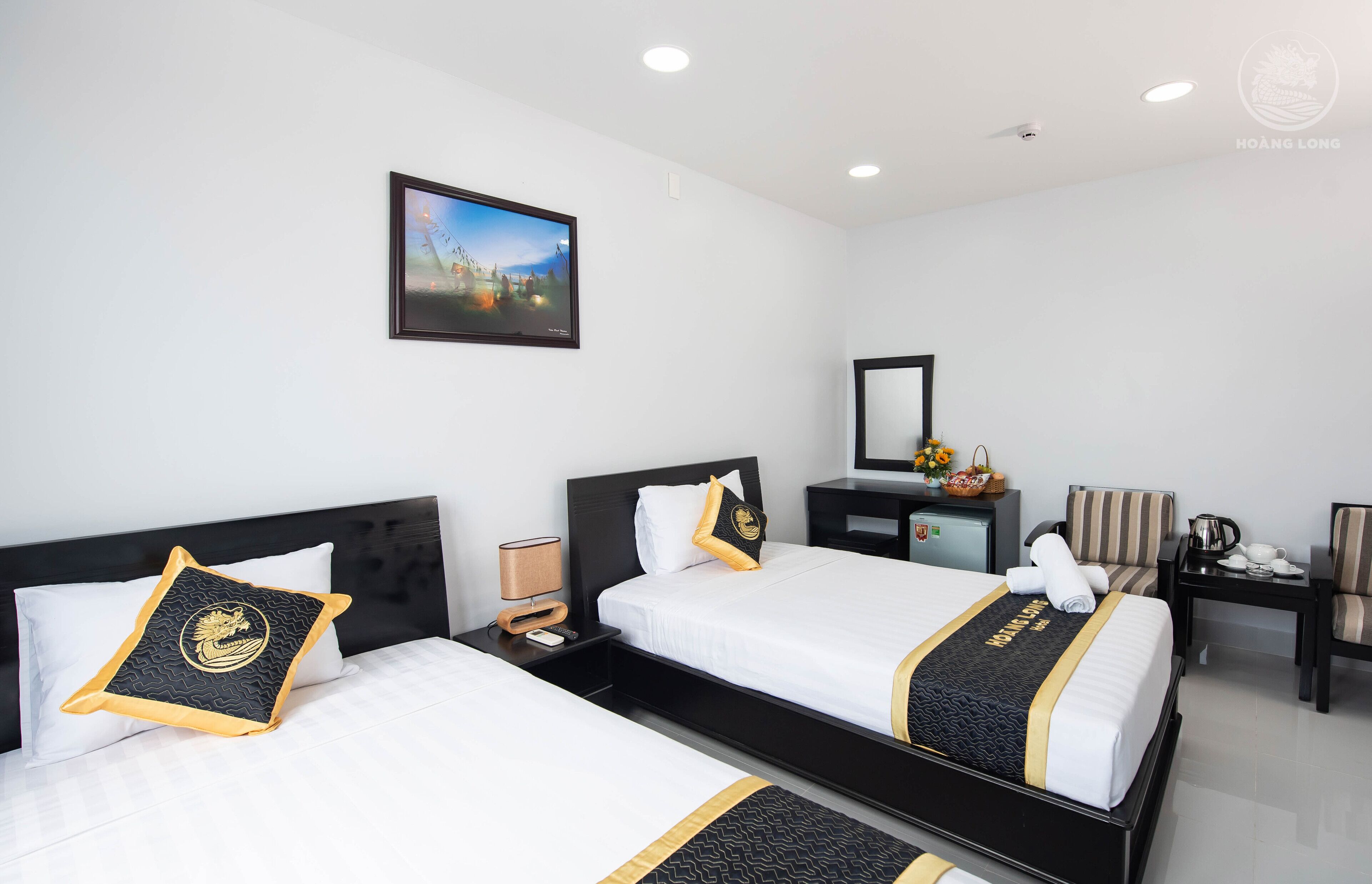 Een hotelkamer met twee bedden, een bureau, een stoel, een nachtkastje, een lamp, een spiegel en een lijst met een afbeelding aan de muur.