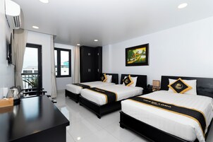 A hotel room with two beds, a desk, a chair, a window with curtains, a painting on the wall, and a view of the outside.