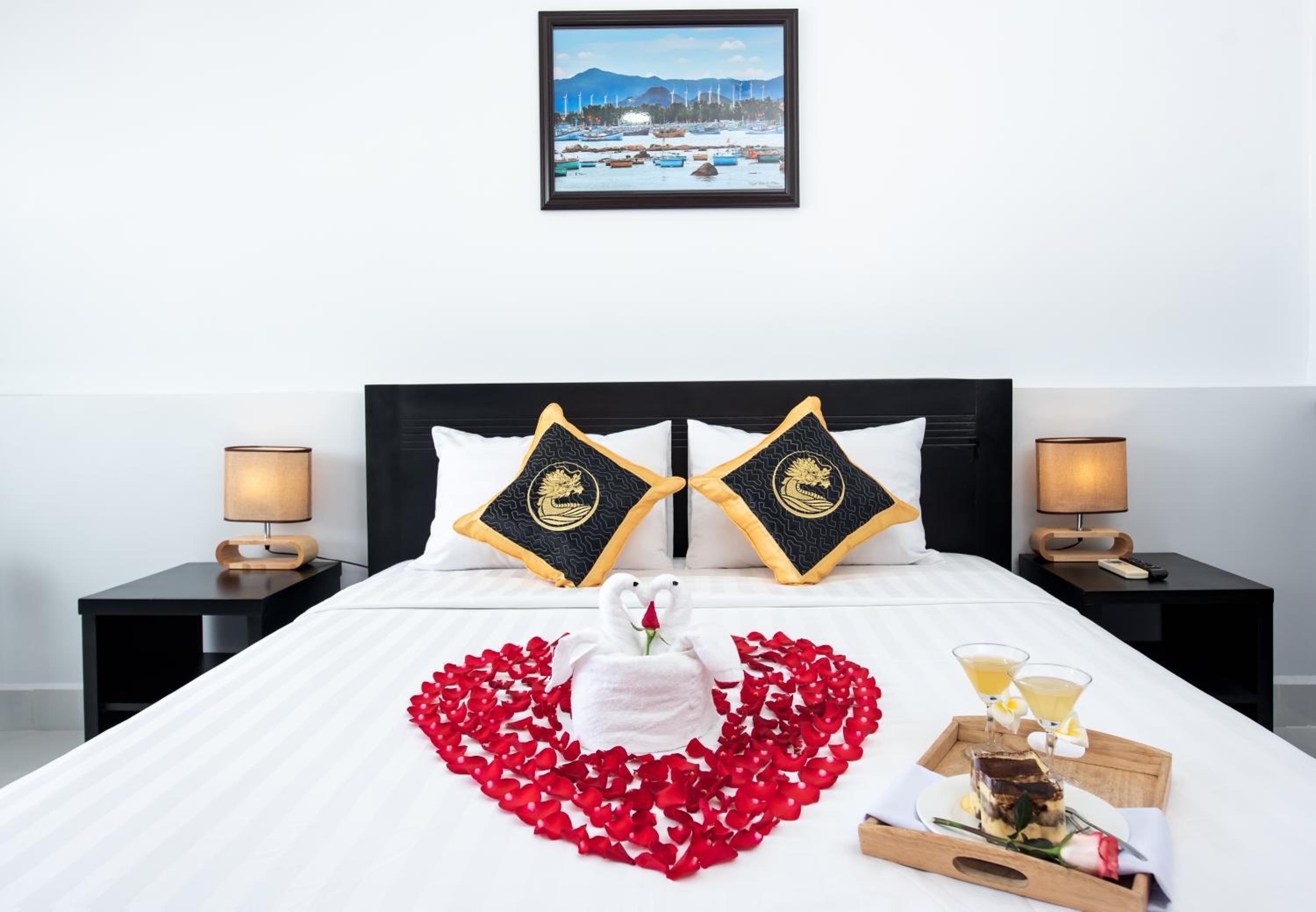 A hotel room with a bed, two nightstands, a framed picture on the wall, and a tray with drinks and a dessert.