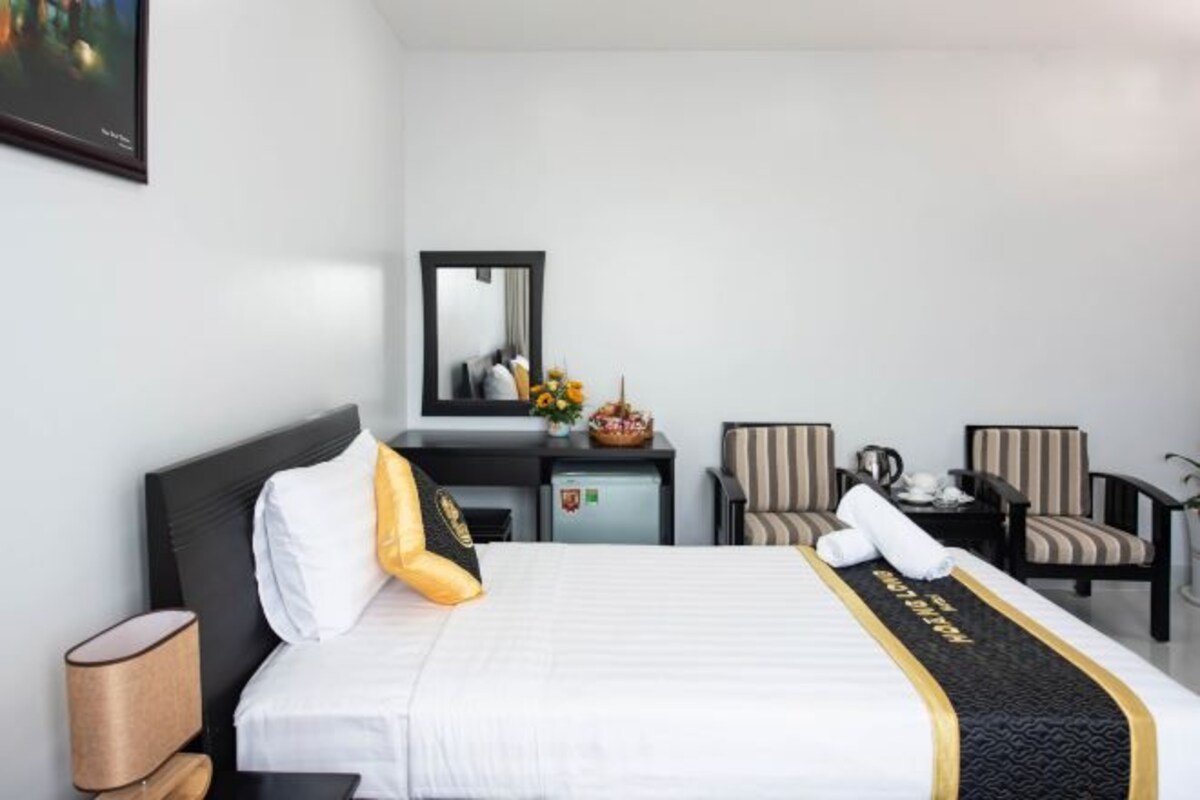 A hotel room with a bed, a desk, two chairs, a small table, and a mirror.