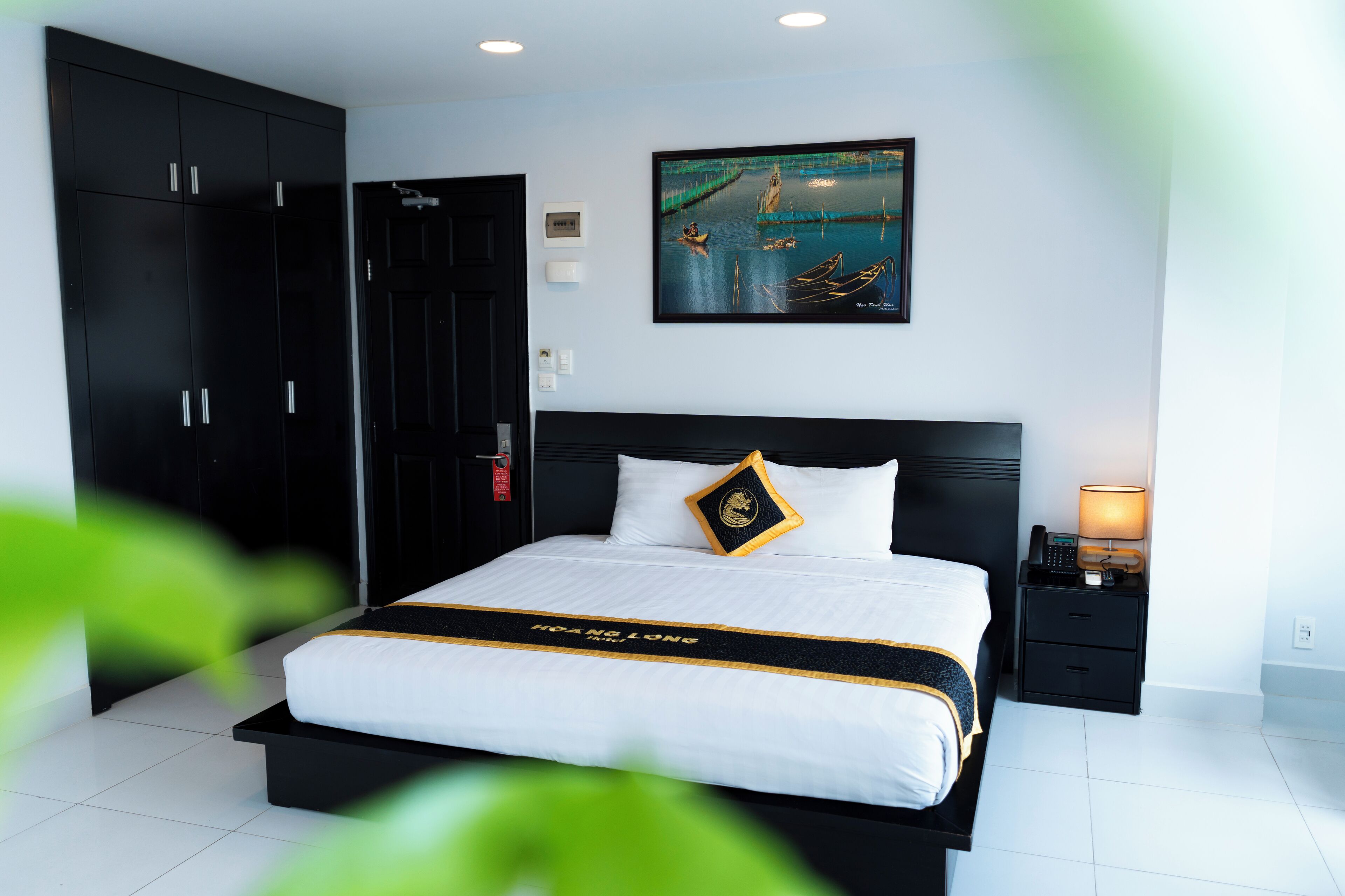 A modern hotel room with a large bed, a nightstand, a painting, and a wardrobe.
