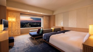 Ein Hotelzimmer mit einem großen Bett, einem Sofa, einem Fernseher und einem Fenster mit Blick auf die Stadt.