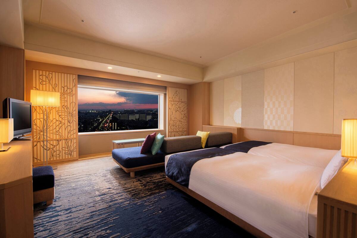Habitación de hotel con una cama grande, un sofá, un televisor y una ventana con vistas a la ciudad.