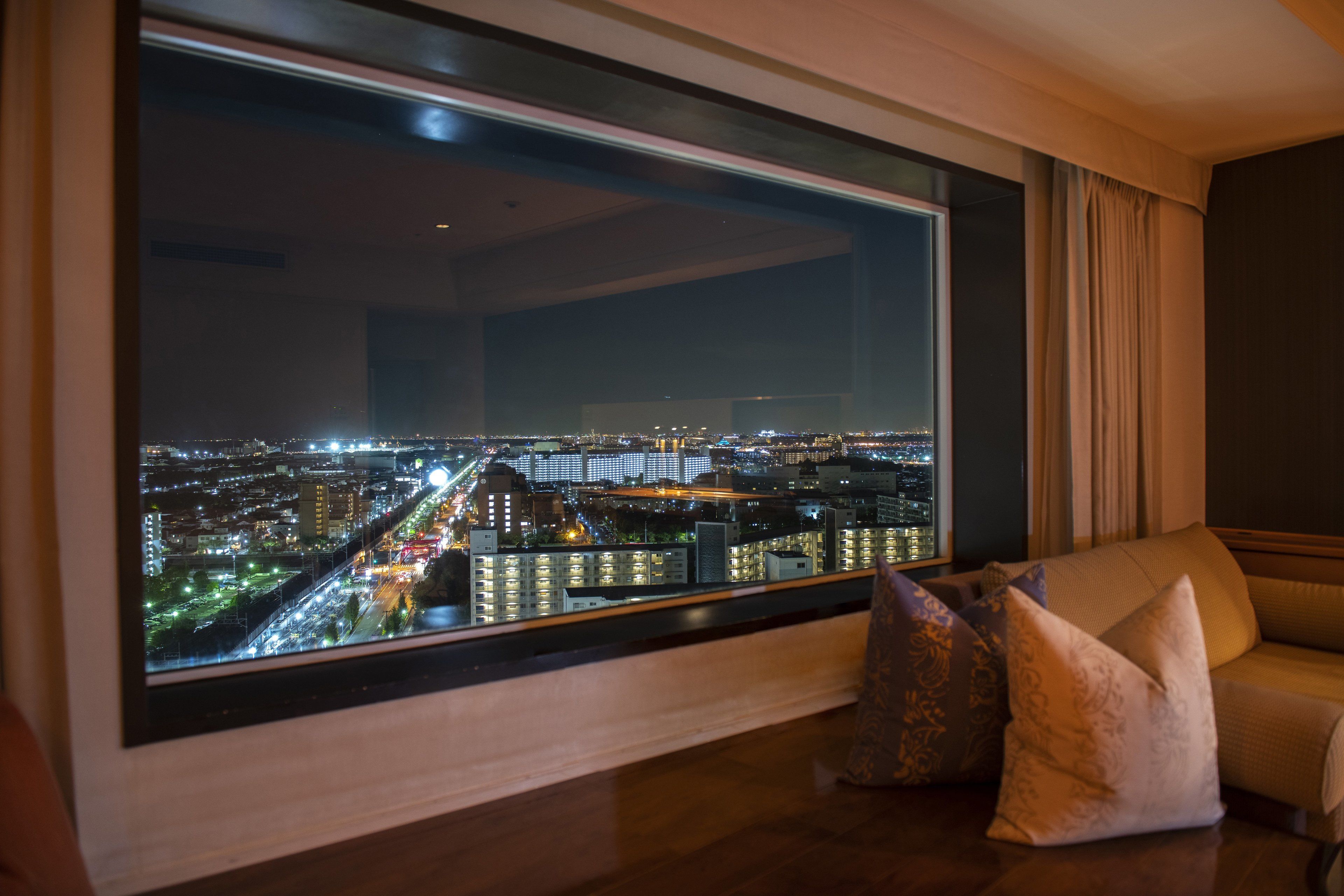 A modern living room with a large window overlooking a cityscape at night.