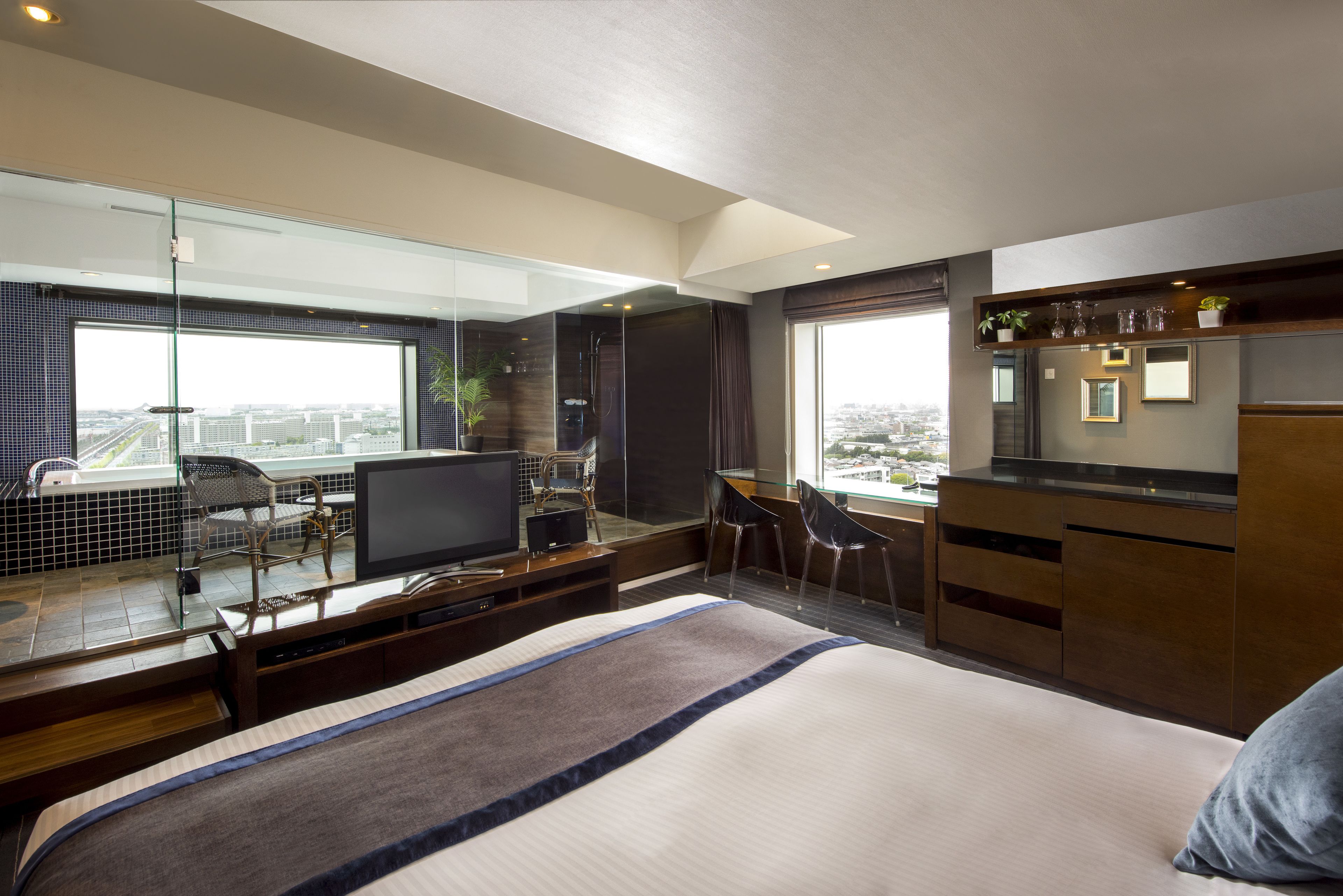 Una habitación de hotel moderna con una cama grande, televisión, escritorio con silla, balcón con vistas a la ciudad y una zona de cocina.