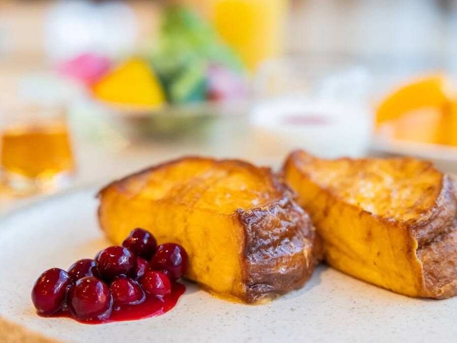 Un plato de desayuno con tostadas francesas, cerezas y un vaso de jugo de naranja.