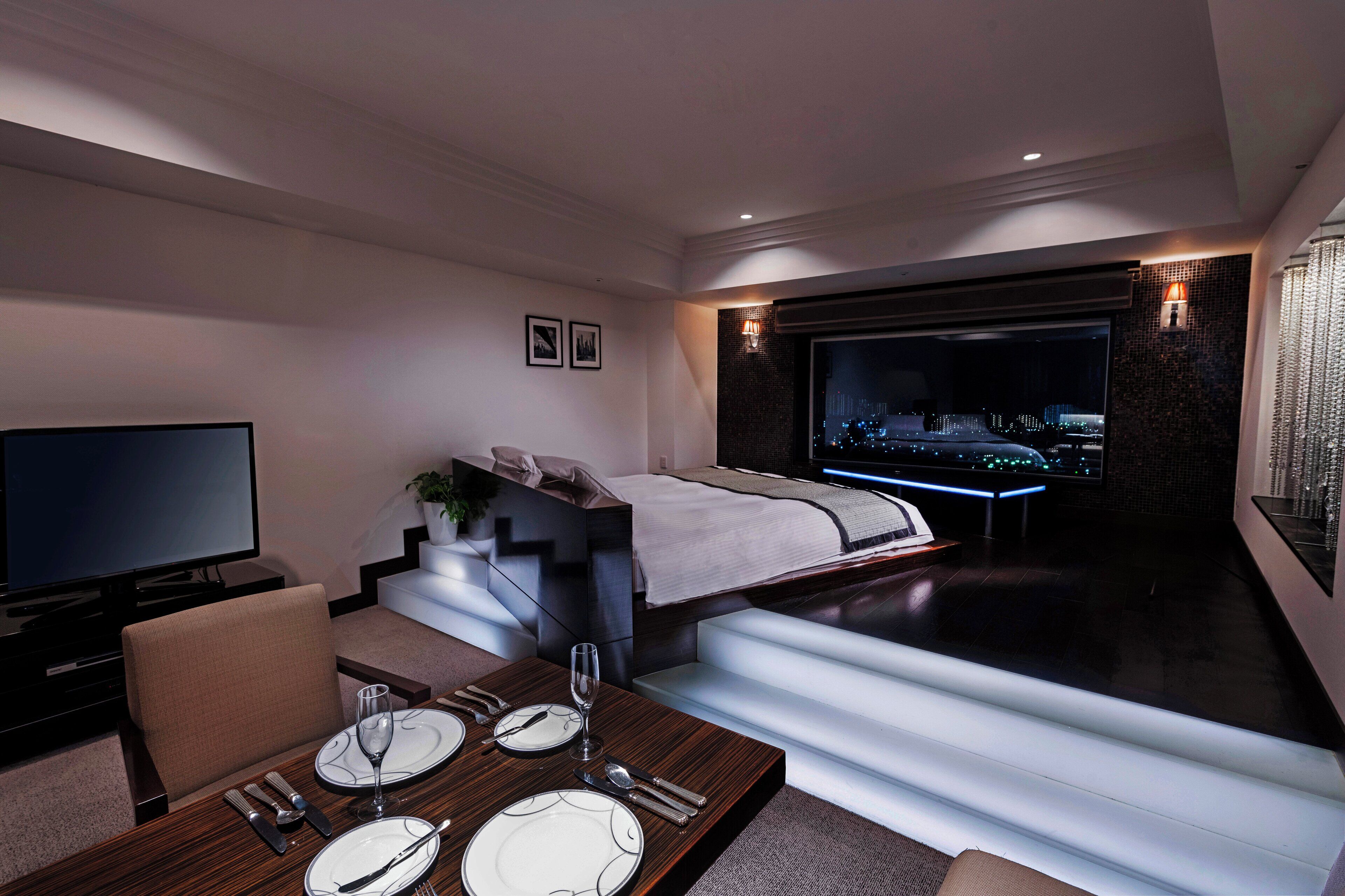 Una habitación de hotel moderna con cama, televisión, zona de comedor y vistas a la ciudad.