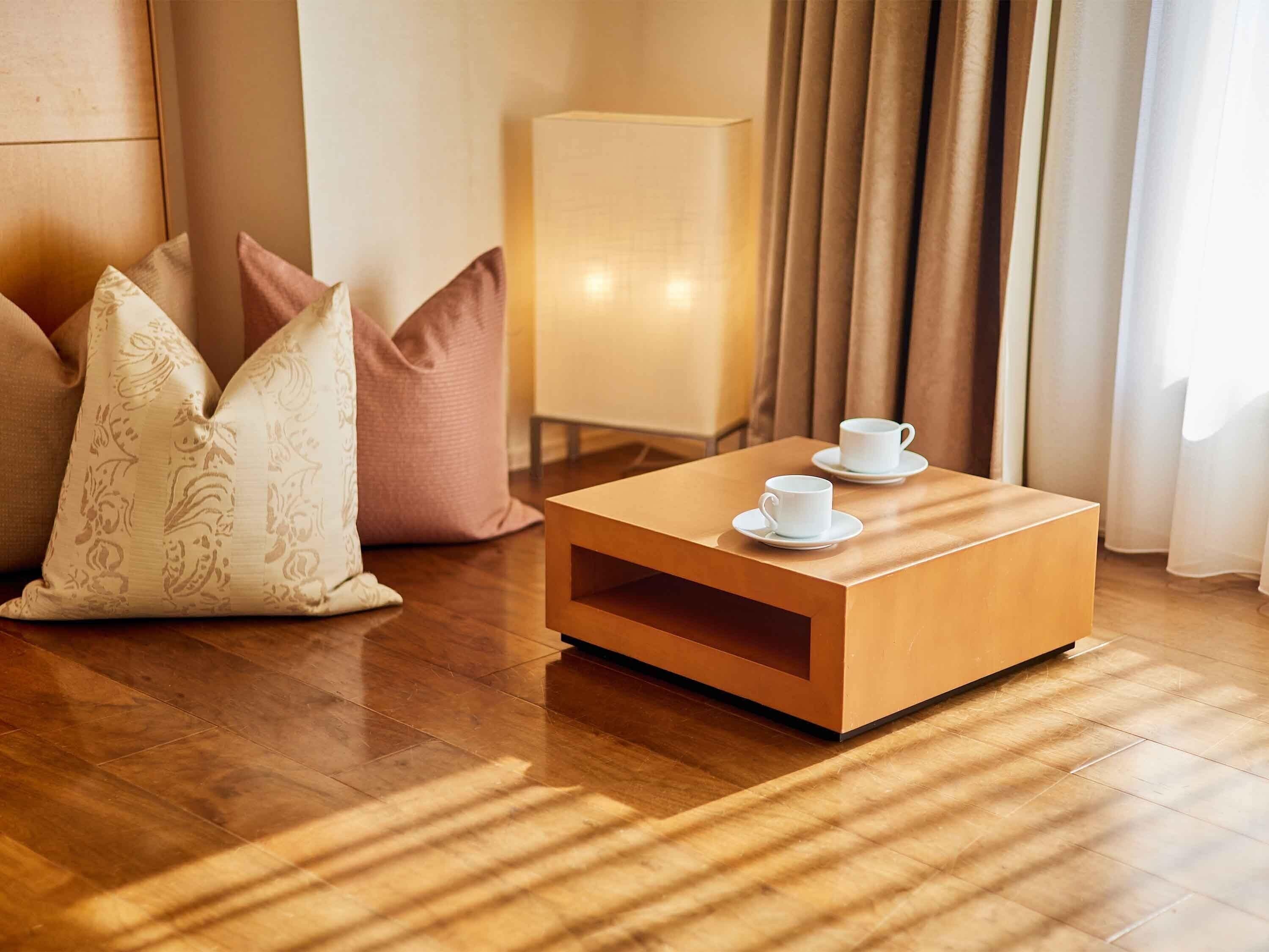 A neatly arranged room with a wooden coffee table, two white cups, and patterned pillows.
