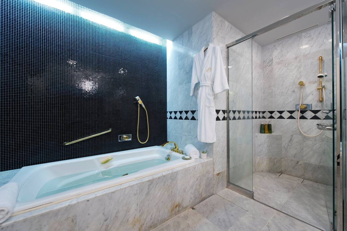 A modern bathroom with a bathtub, a glass-enclosed shower, and a tiled wall with a geometric pattern.